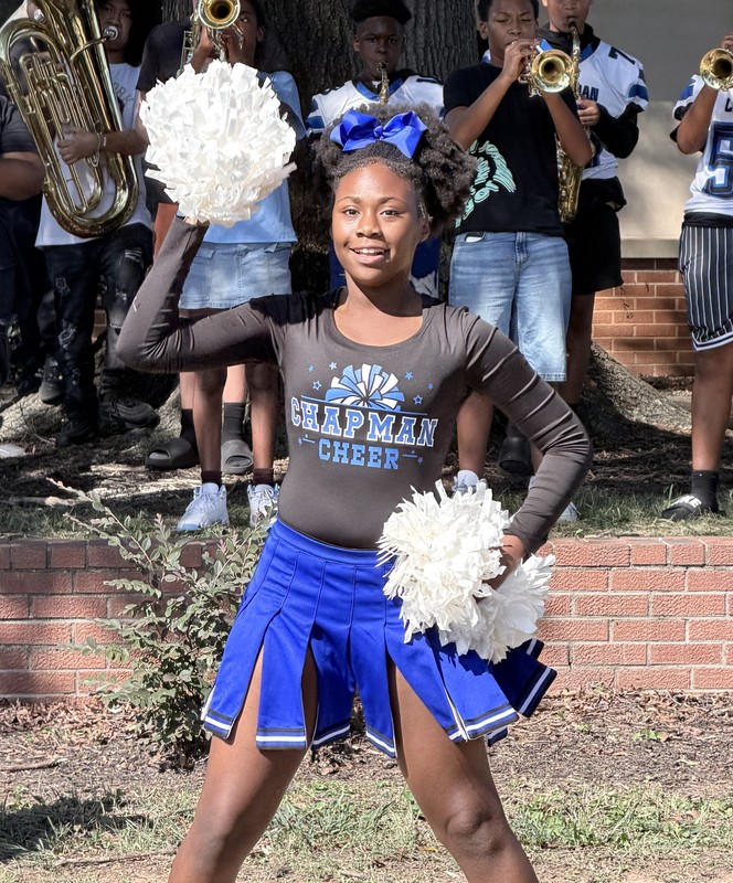 A cheerleader is leading the crowd during the pep rally in the courtyard with the band playing behind her.