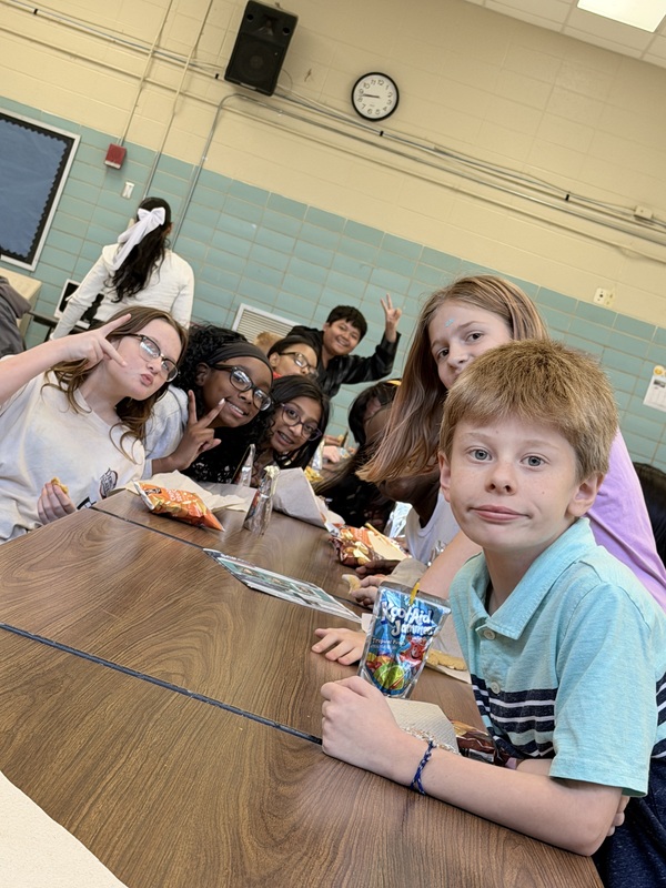 Students are gather around the end of the table as they enjoy their cake and cookies during the attendance celebration.