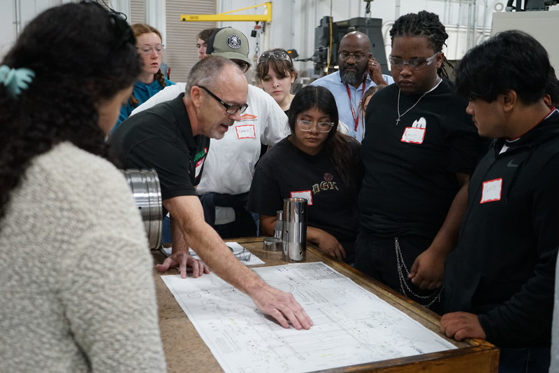 Welding and precision machining students look at a diagram while the Bruderer employee explains what is on the paper.