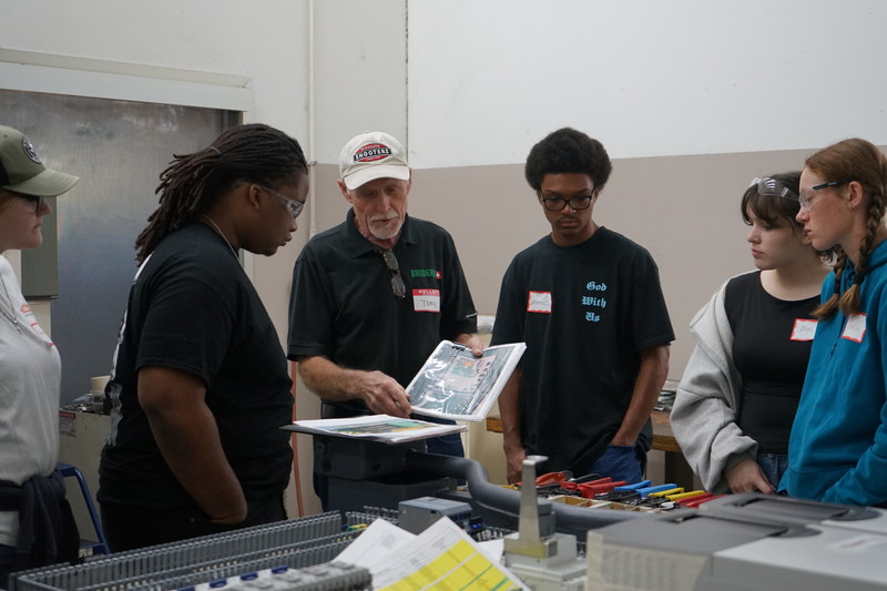 Bruderer employee pointing out machine diagrams to welding and precision machining students from a book