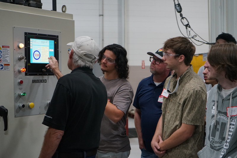 Welding and precision machining students look on as a Bruderer employee works a machine.