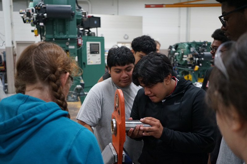 Welding and precision machining students attempt to place a piece of machinery into a hole.