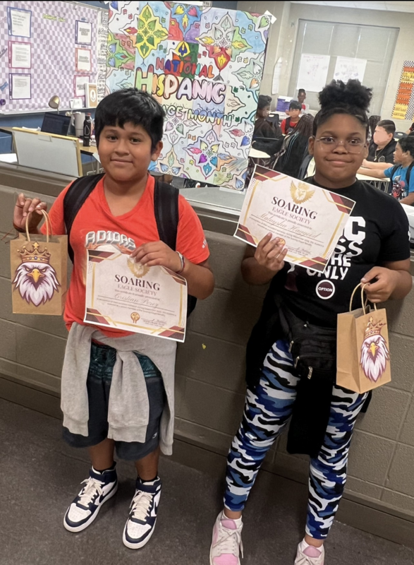 A boy and a girl hold up their Soaring Eagles certificates and goody bags