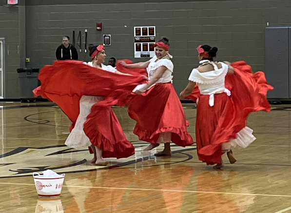 Three women in traditional dress demonstrate an Afro-Latin dance