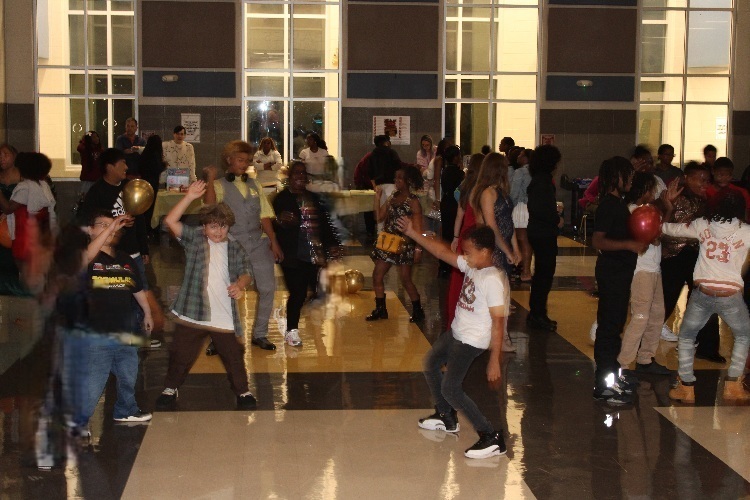 A large group of kids dacing in the middle of the lunchroom