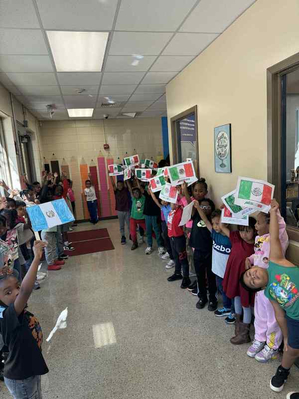 2nd grade in the hall representing their country, Mexico, by holding up flags getting ready to join the parade.