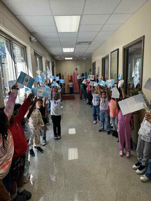 1st grade in the hallway representing their country, Guatemala, by holding up the Guatemala flag waiting to join the parade.