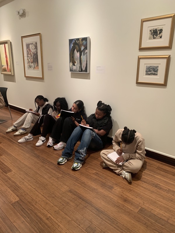 Several students sitting on the floor, focused on a vibrant painting displayed in front of them.