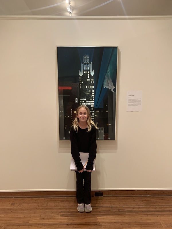 A young girl smiling in front of a vibrant painting in a gallery setting.