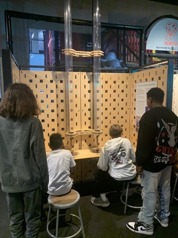 A group of people gathered around a table in front of a wooden wall, engaged in conversation or discussion