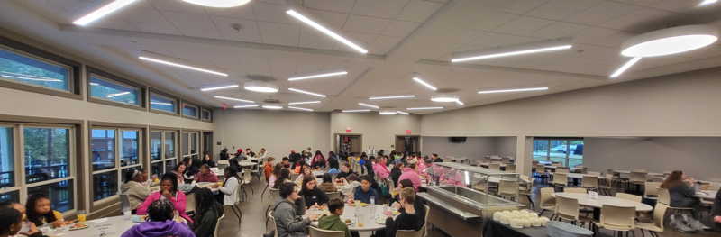 A crowd of scholars sitting at tables in an expansive room, involved in various conversations and activities.