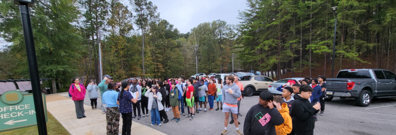 A group of scholars standing together in a parking lot, engaged in conversation.