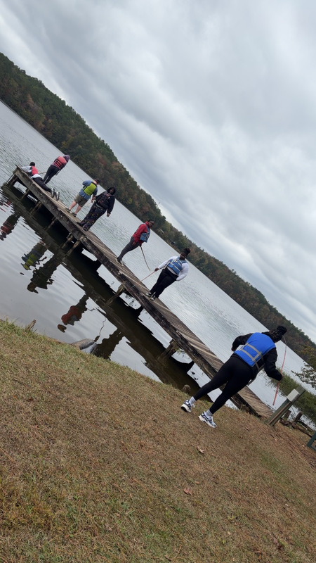 Several individuals gather on a dock beside a lake, engaging in conversation and fishing