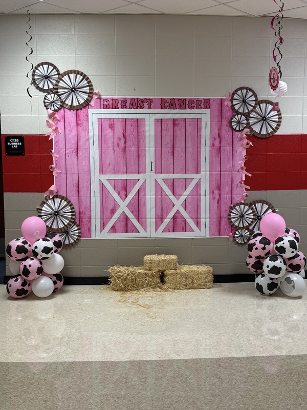 Pink and White barn mural on the wall with 2 wheels hanginfg on each top corner with pink and white balloons with brown specks on each bottom corning and three stacks of hay in the middle