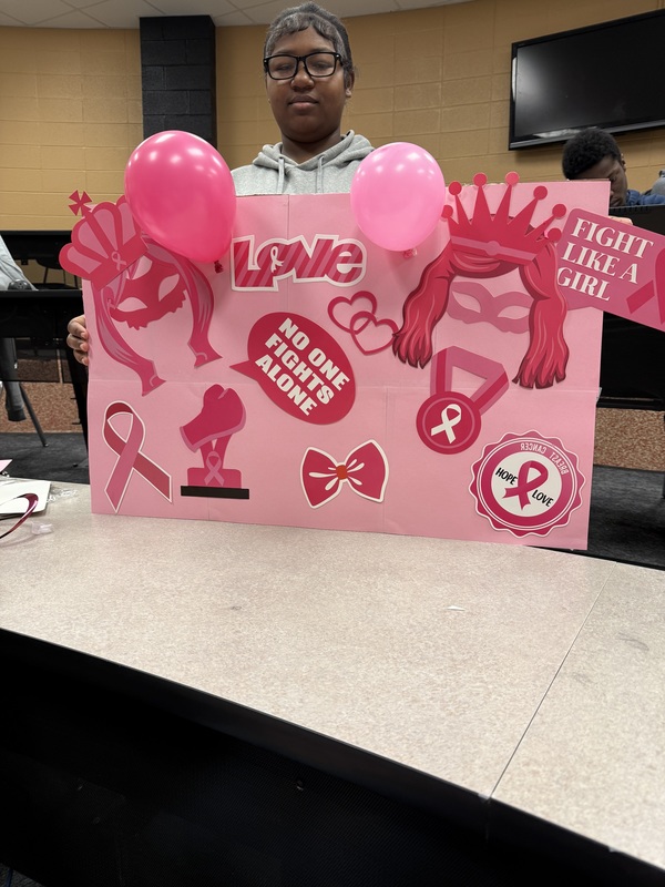 Student standing and holding up a pink poster with balloons and ribbons with white writing