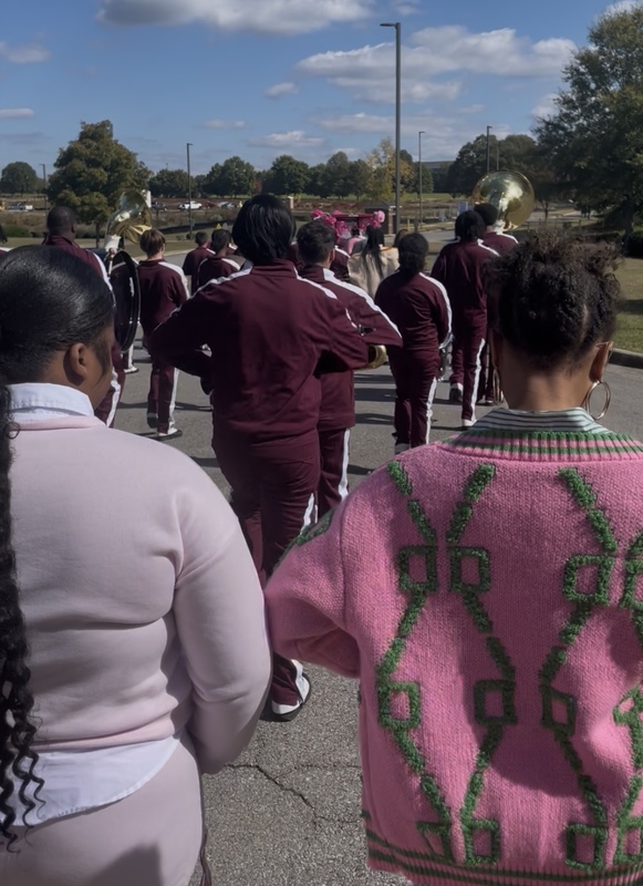 Two people dressed in pink and white, pink and green walking behind the Columbia band wearing marron and white uniforms playing instruments for breast cancer awareness walk