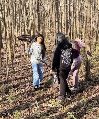Three girls collect soil samples from the forest floor.