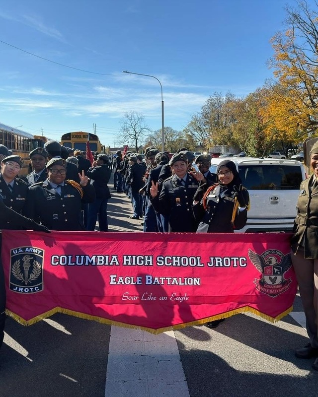 JROTC Eagle Battalion holding up red banner with army logo and Columbia High School Eagle Batallion in white letters walking downtown Huntsville in Vets day parade