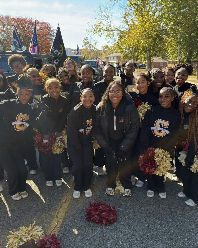 Columbia High Cheerleades in black gold and white jogging suits with white tennis shoes and marron and gold pom-poms on street in front in front of them as they pose for group picture