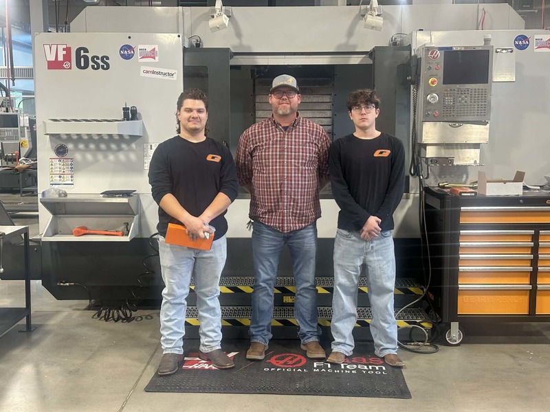 Machining students pose with their machining instructor in front of a large CNC machine