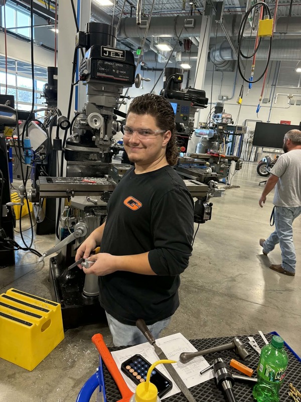 Josh Williams smiles in front of a machine at the machining competition