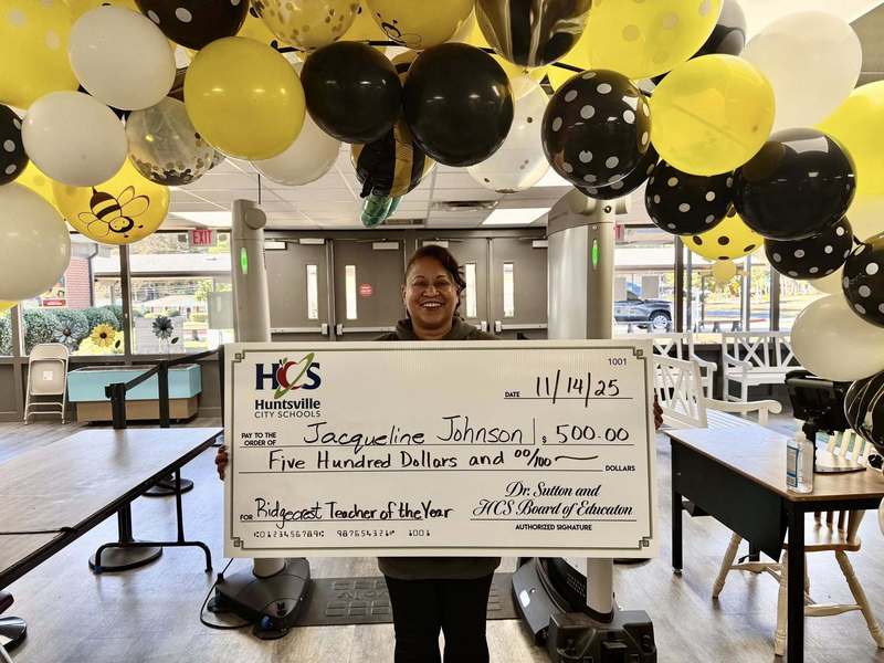Teacher Jackie Johnson posing with a large check under balloon decorations