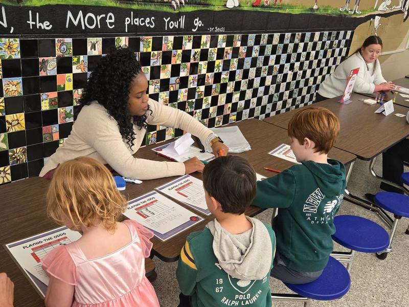 teacher sitting at table with kids playing math games