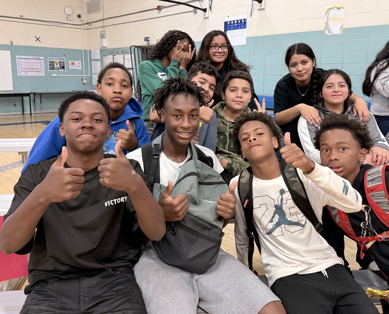 Students are smiling and showing support during the Hispanic Heritage Celebration at Chapman. The group of students are sitting on the bleachers in the gym.