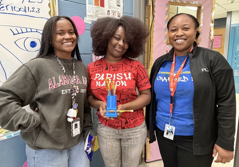 Ms. Hampton and Ms. Moncur pose with Amara who is displaying the paint brush holder she designed and created for art classes.