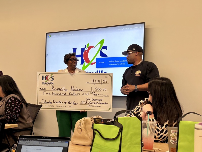 Mrs. Holman standing in front of white board with HCS logo holding a big check written out to her for $500 for Teacher of the year and principal, Dr. Richey standing next to her