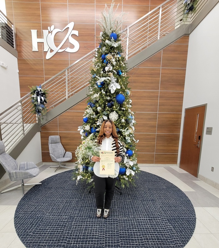 Tamarion Kelly staing in HCS Board of Education foyer in front of decorated Christmas tree 
