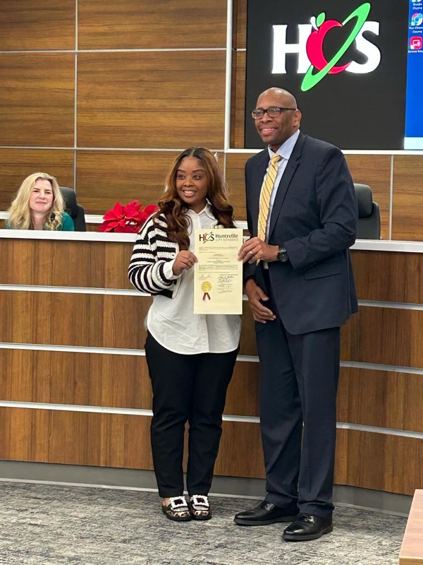 Tamarion Kelly holding award certificate with Superintendent Dr. Sutton at the Board of Education