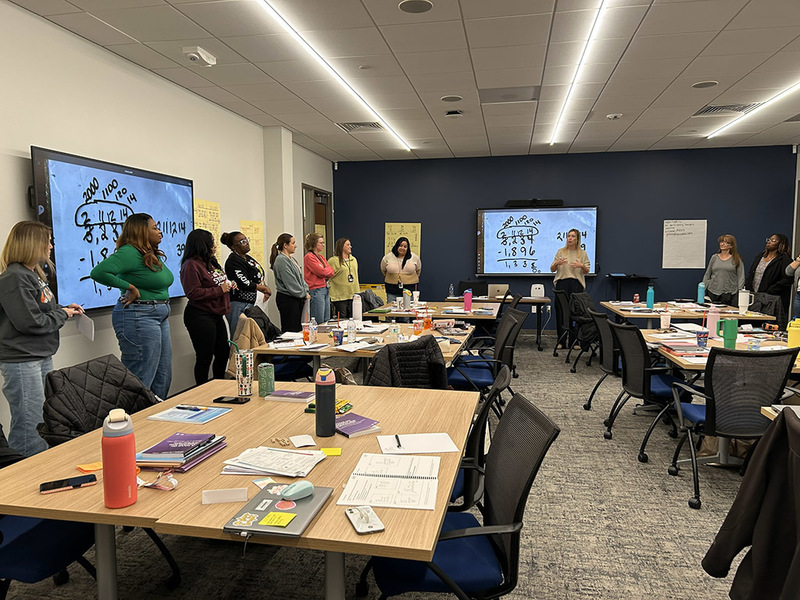 Teachers standing around the edges of ther oom while working on a group activity