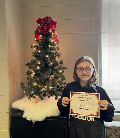 Spelling Bee champion poses with his certificiate next to a small Christmas tree. 