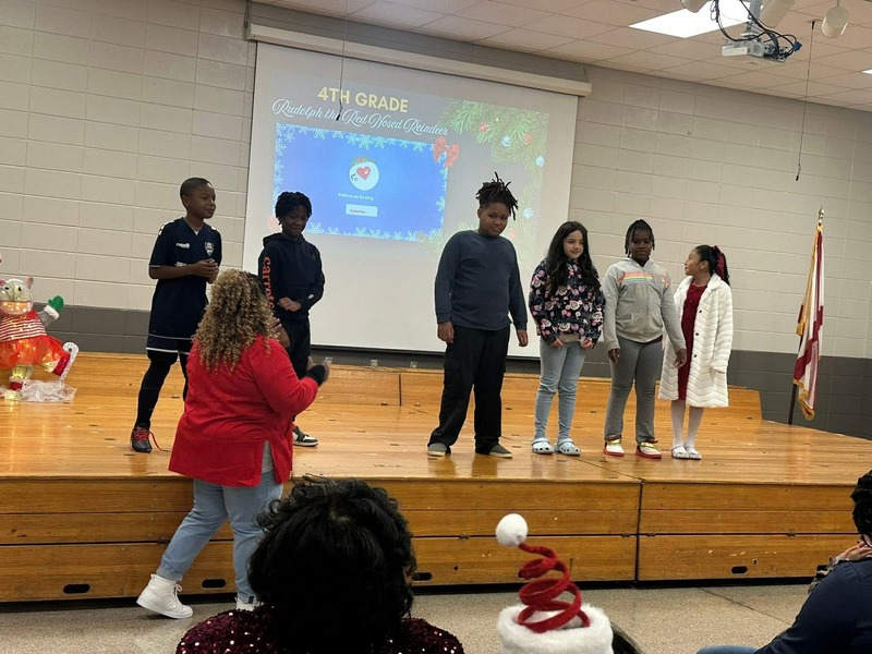 4th grade students on the stage singing "Rudolph the "Red Noised Reindeer."