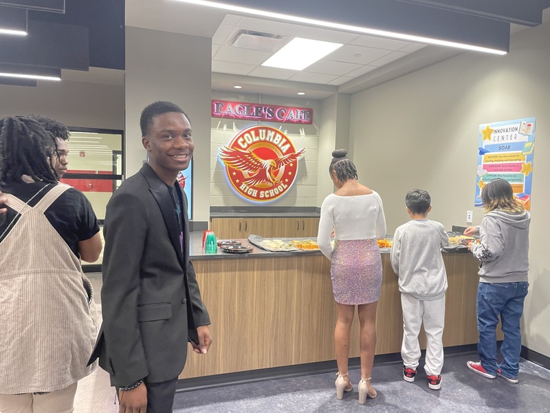 Six students standing in front of the Eagle's Cafe at Columbia plating food and some looking on