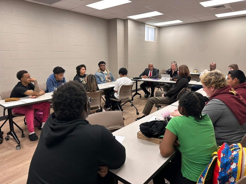 Student leadership team sitting at white tables with superintendent and principal discussing concerns and issues