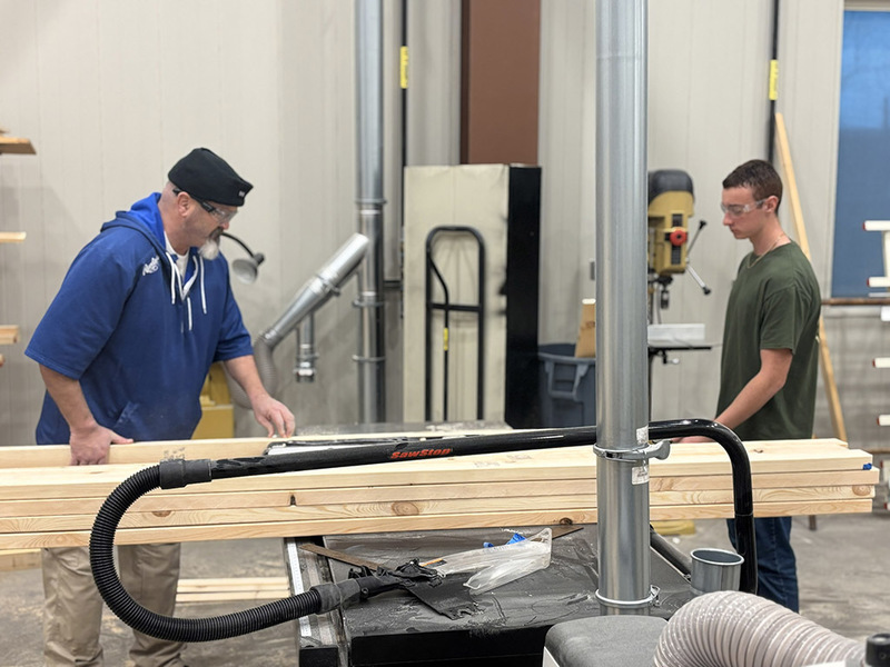 Teacher and student work together to cut a board