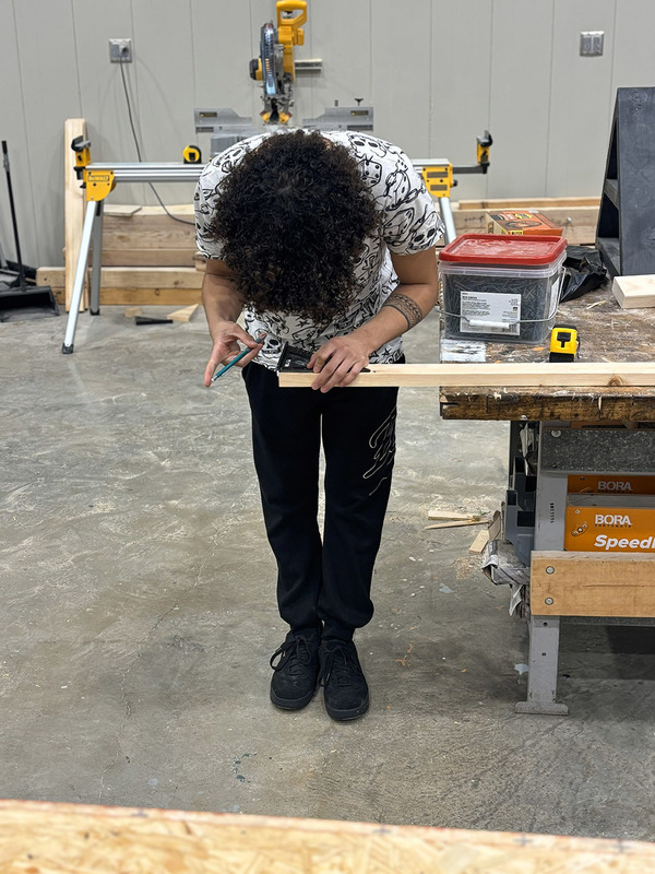 Male student leans over a 2x4, marking his cut