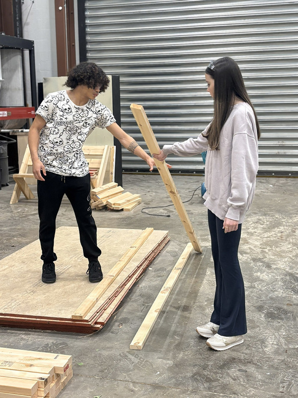 Male student handing a 2x4 to a female student