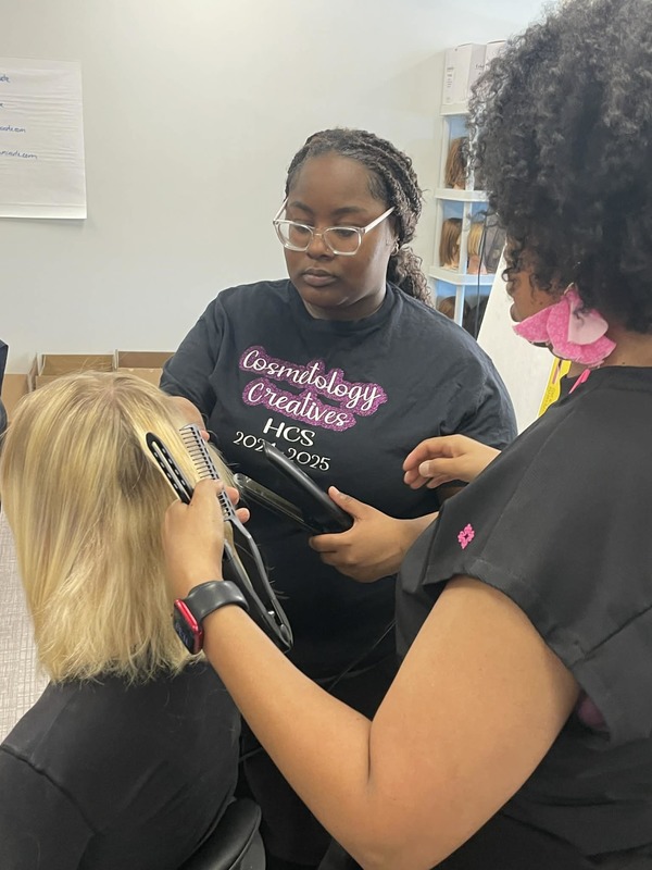 Cosmetology student works with the flat iron on another student's hair. Mrs. Johnson, the Cosmetology teacher is hands on supervising. 