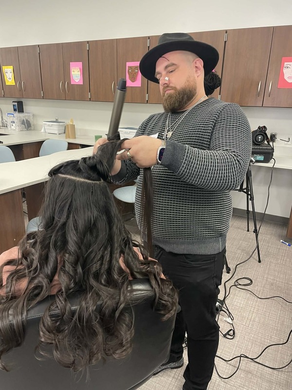 J.T. Reed utilizing the curling iron on a student's hair