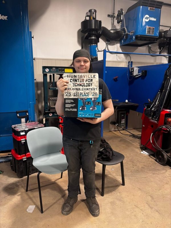 Winner of the welding competition holds up a sign that says Huntsville Center for Technology Welding Contest 1st Place. 