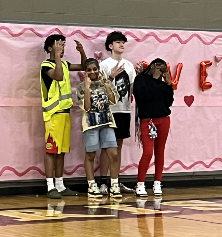 Two couples stand in front of a pink banner with the word LOVE on it