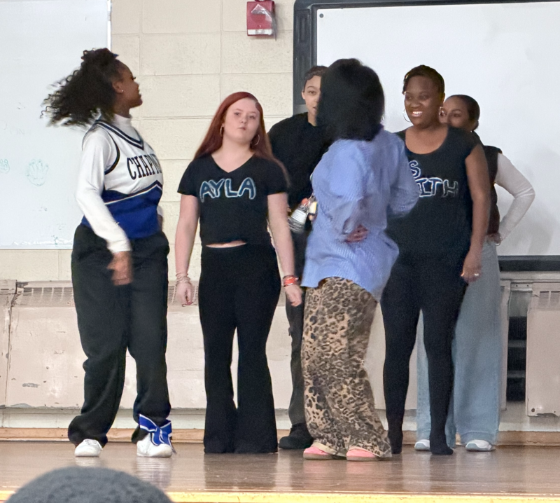 A group of students and staff dance on the school’s stage. Each student and staff member is paired with another to showcase their dance skills. 