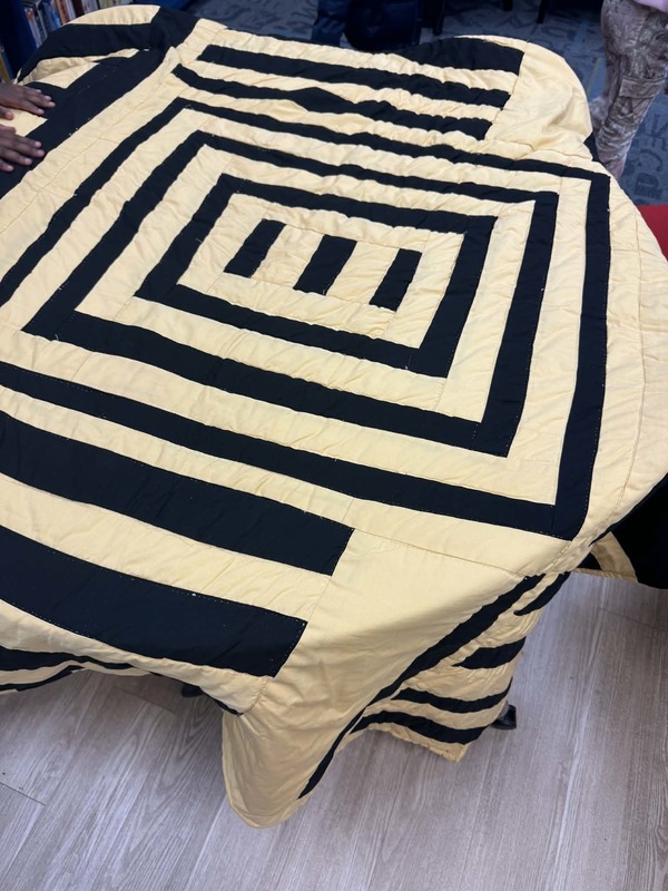 A quilt that is yellow with black stripes all around. It looks like a maze.
