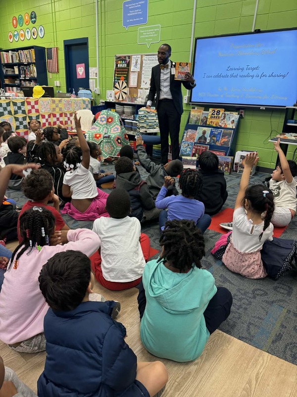 Mr. Saulsberry standing up in the library asking the students which book he should read first.