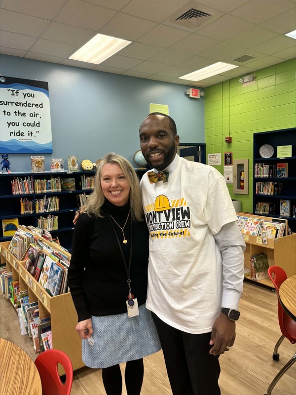 Principal Sutton and Larry Saulsberry wearing a Montview shirt in the library.