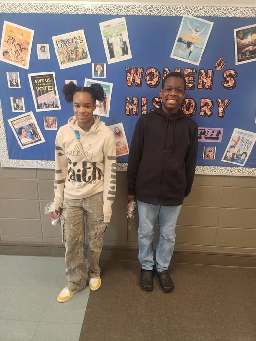 Two students stand in front of a bulltein board. 