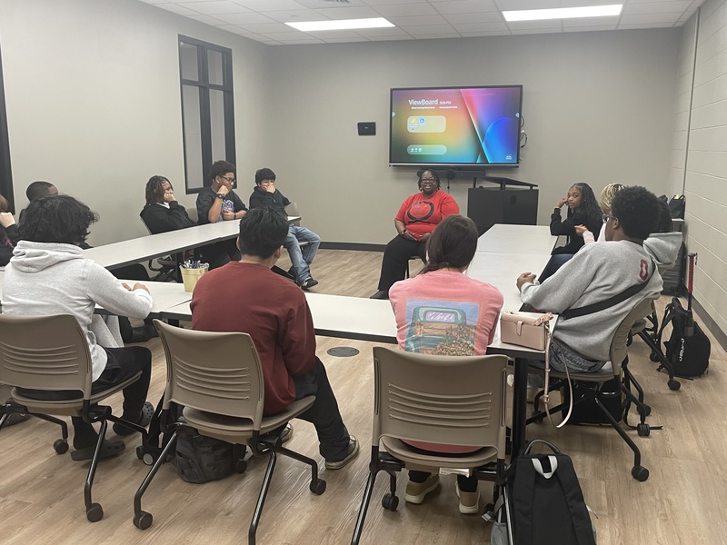 Dr. Royston talking to a group of students sitting around table in conference room